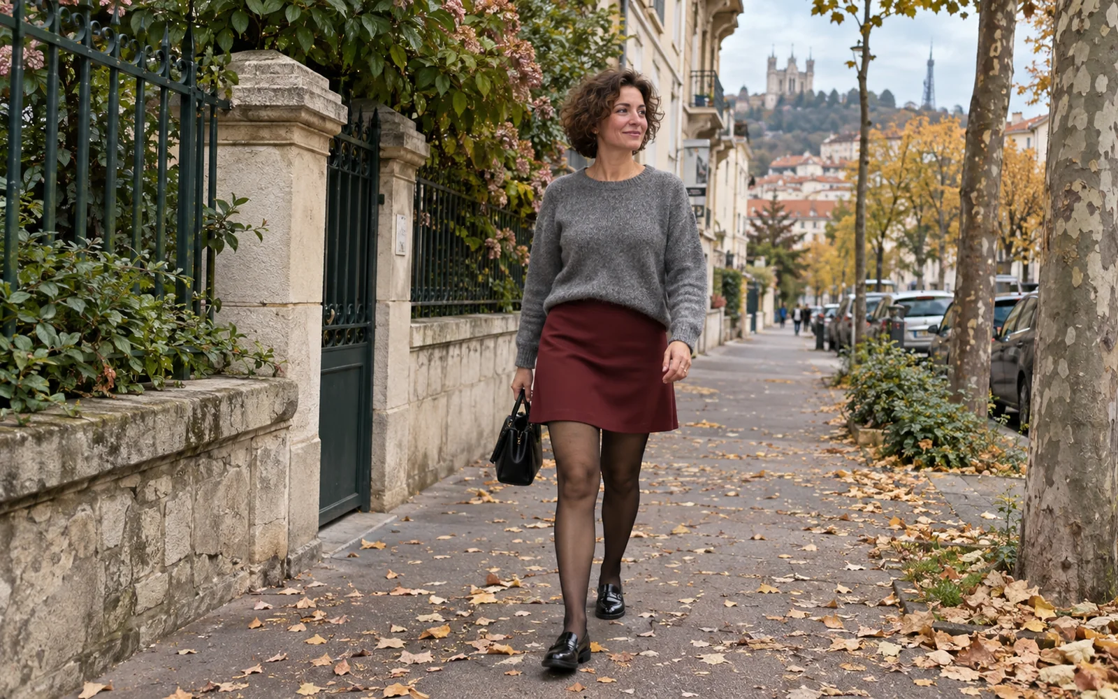 Femme en pull gris, jupe bordeaux, collants noirs fins et mocassins noirs dans une rue