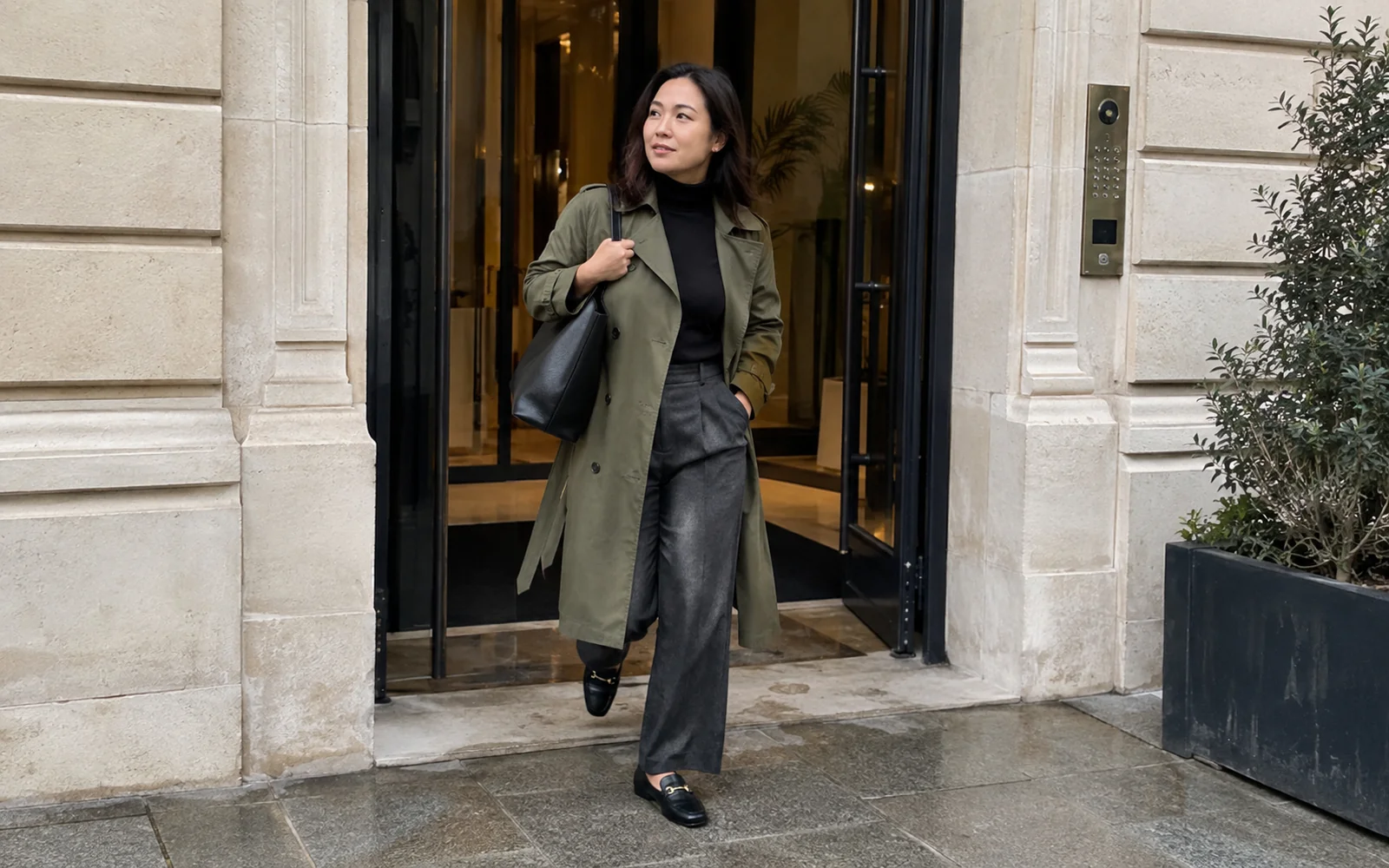 Femme en trench kaki ouvert, col roulé noir, pantalon large anthracite et mocassins, devant un immeuble de bureaux