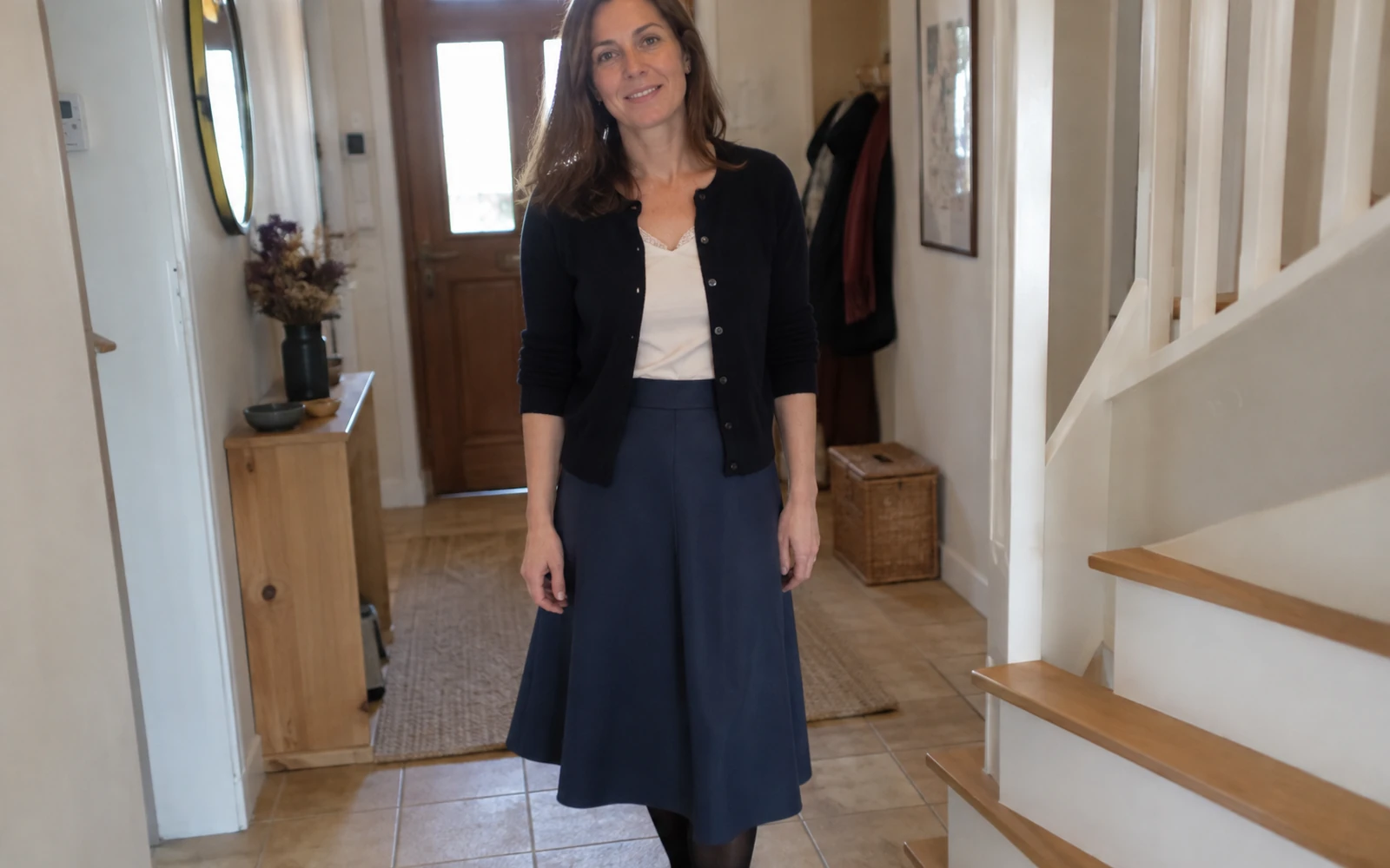 Femme portant une jupe midi et un cardigan dans une entrée.