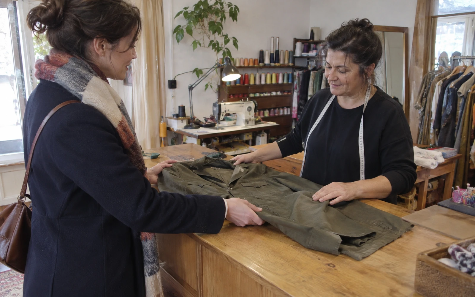 Deux femmes regardent une veste kaki sur la table d’un atelier de couture.